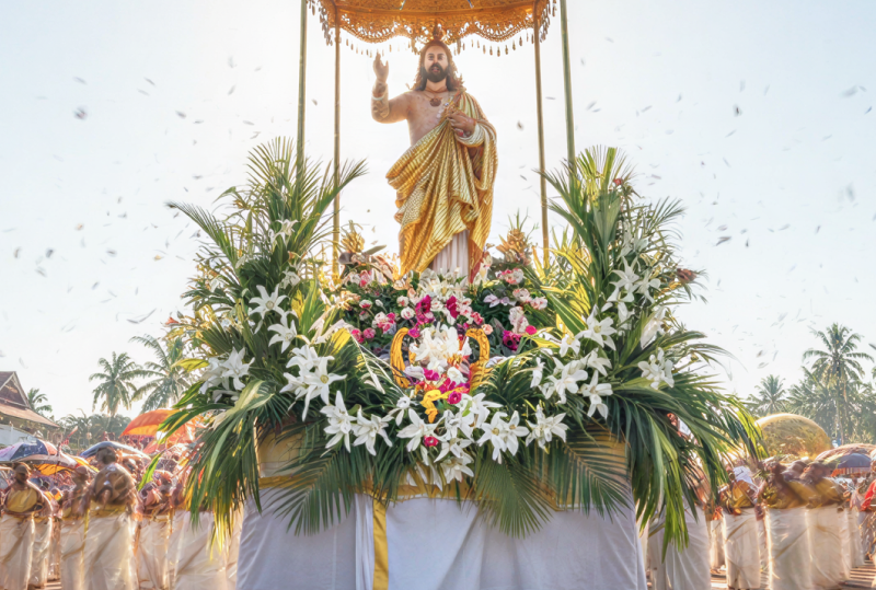 A festive Easter in Kerala procession featuring a floral float with a Jesus statue, devotees in white attire, and colourful ceremonial umbrellas thumbnail