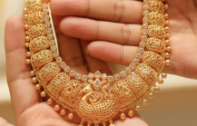 Hands holding an intricate traditional gold necklace with peacock motif and ruby accents, representing the experience of buying gold in India thumbnail