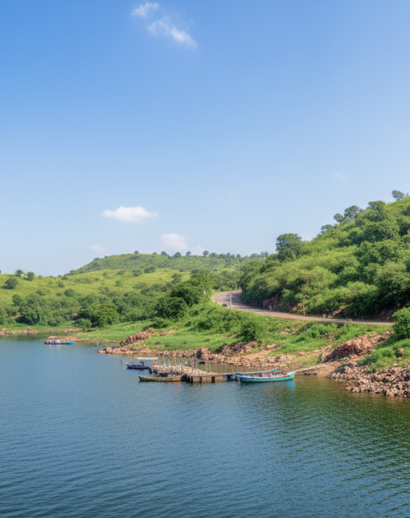 A calm blue lake surrounded by green hills with small boats docked near the shore, a scenic stop on a day Pune itinerary thumbnail