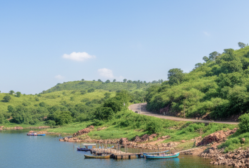 A calm blue lake surrounded by green hills with small boats docked near the shore, a scenic stop on a day Pune itinerary thumbnail