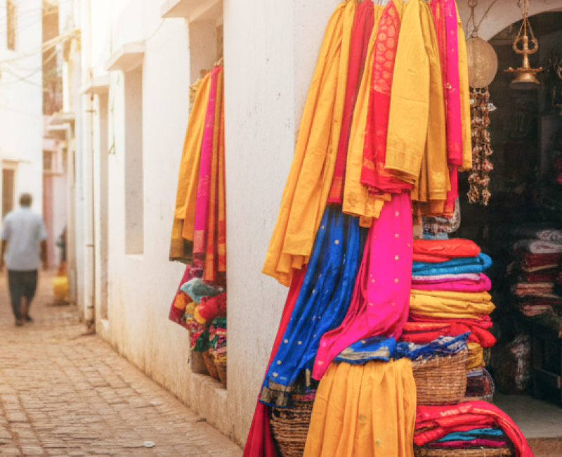 A colourful hidden shopping gem in Pondicherry — vibrant sarees and brass goods spilling out of a tiny stall tucked into a narrow whitewashed lane thumbnail