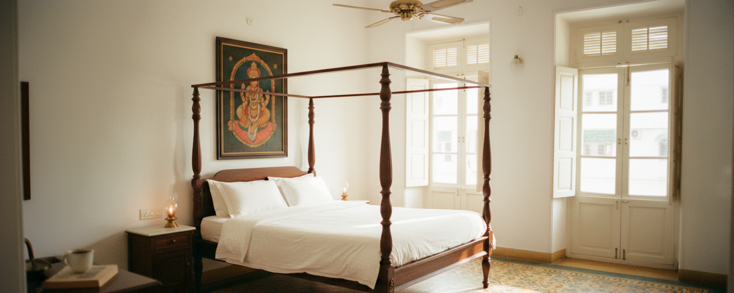 Charming stay in Pondicherry — a colonial four poster bedroom with white linen, Athangudi tiled floors, brass oil lamps, and a Tanjore painting above the bed