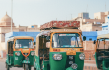 Green and yellow auto rickshaws driving along a cobblestone street toward a historic stone archway in an India thumbnail