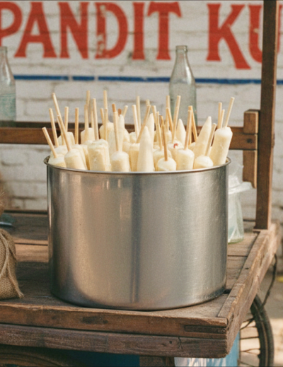 Pandit Kulfi stall in Jaipur with a metal pot filled with traditional kulfi ice cream sticks on a wooden street cart thumbnail