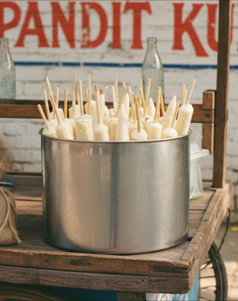 Pandit Kulfi stall in Jaipur with a metal pot filled with traditional kulfi ice cream sticks on a wooden street cart thumbnail