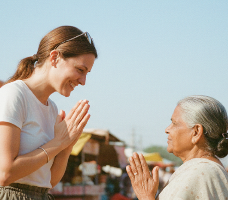 Traveler greeting a local woman with a namaste gesture at a colorful street market in India thumbnail