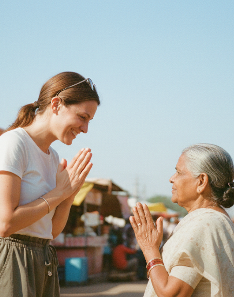 Traveler greeting a local woman with a namaste gesture at a colorful street market in India thumbnail