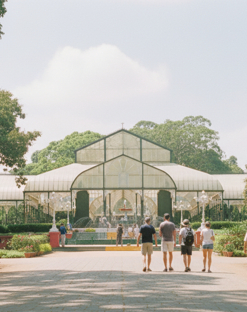 day Bangalore itinerary stop at Lalbagh Botanical Garden — visitors walking toward the iconic Glass House surrounded by century old trees and rose beds thumbnail
