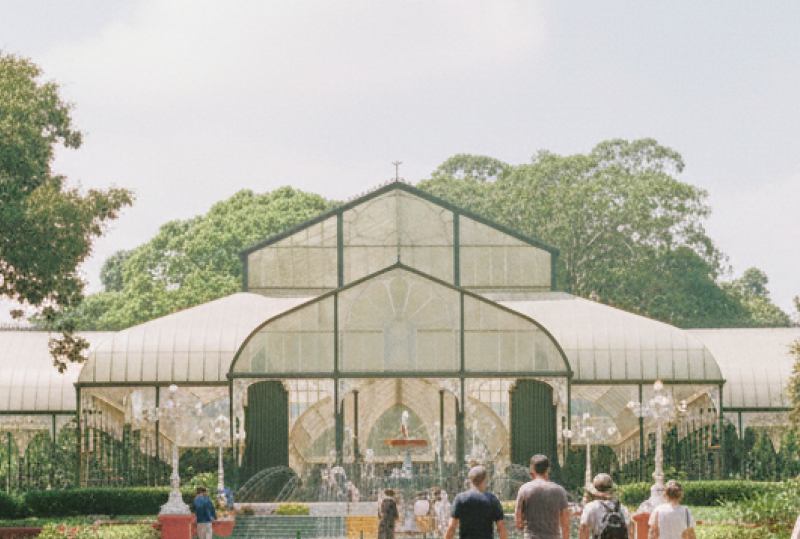 day Bangalore itinerary stop at Lalbagh Botanical Garden — visitors walking toward the iconic Glass House surrounded by century old trees and rose beds thumbnail