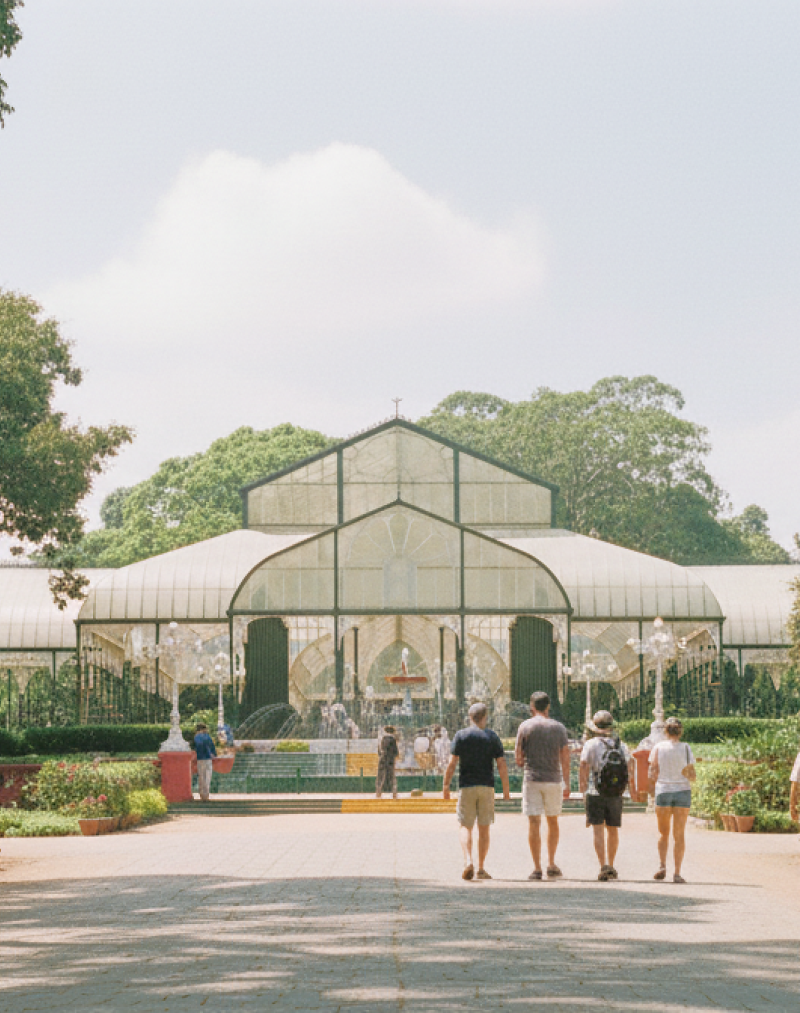 day Bangalore itinerary stop at Lalbagh Botanical Garden — visitors walking toward the iconic Glass House surrounded by century old trees and rose beds thumbnail