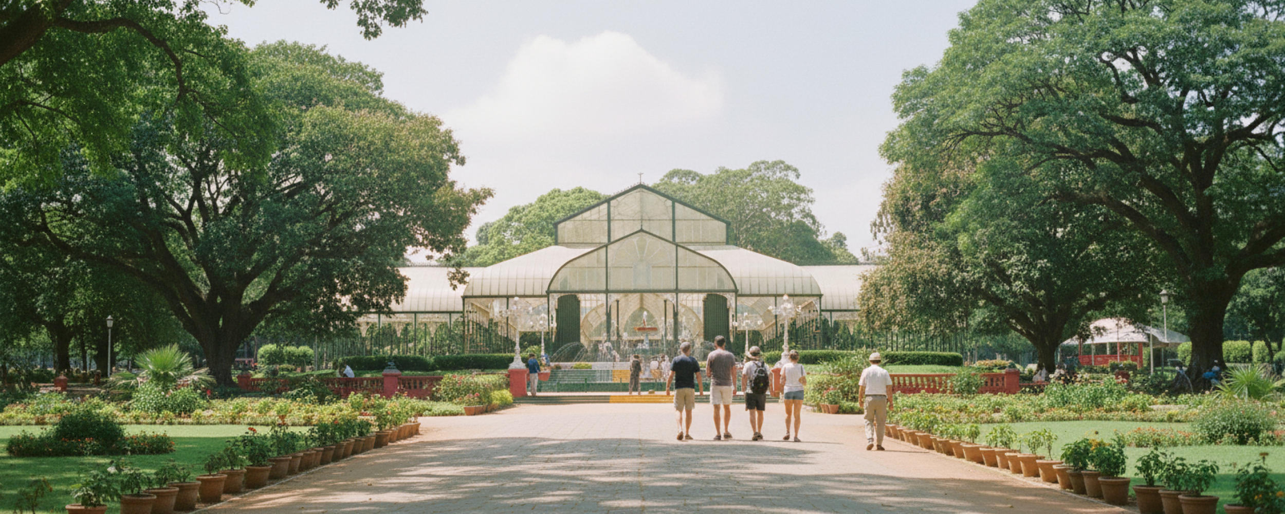 day Bangalore itinerary stop at Lalbagh Botanical Garden — visitors walking toward the iconic Glass House surrounded by century old trees and rose beds