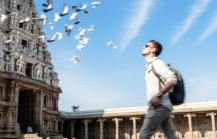 A Caucasian tourist walking through the courtyard of Kapaleeshwarar Temple in Chennai, with pigeons in flight against a vivid blue sky — Chennai travel guide thumbnail