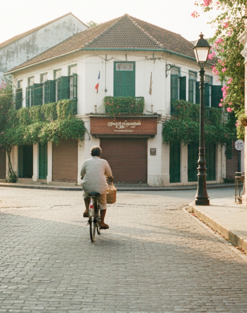 A cyclist rides through an empty cobblestone street in Pondicherry's White Town at golden hour, flanked by colonial buildings and bougainvillea — captured in this Pondicherry travel guide thumbnail