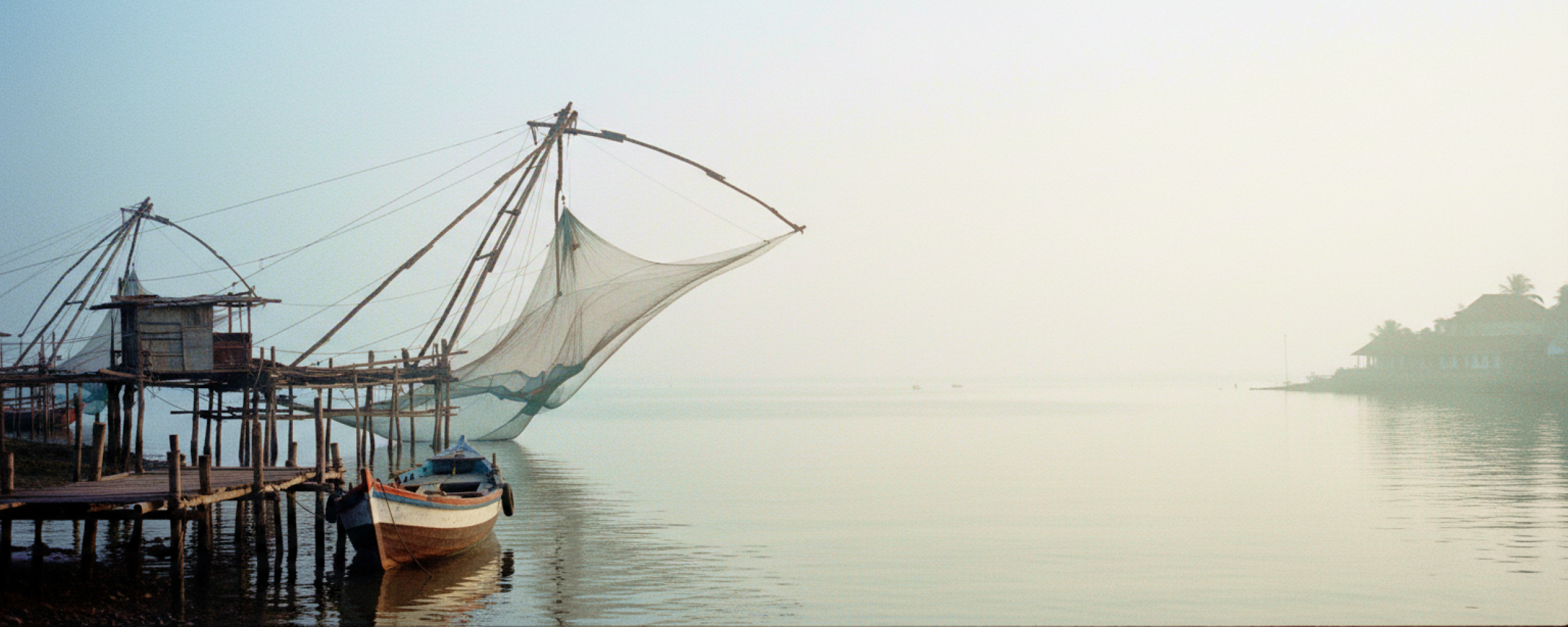 Chinese fishing nets and a weathered wooden boat on the misty Fort Kochi waterfront at dawn — a highlight of any day Kochi itinerary