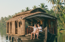 Two tourists on a traditional houseboat drifting through the palm lined backwater canals near Kochi — a must do experience covered in this Kochi travel guide thumbnail