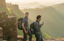 Two travellers with backpacks standing on the ramparts of Sinhagad Fort at sunrise, overlooking the misty Western Ghats — a highlight of any Pune itinerary thumbnail