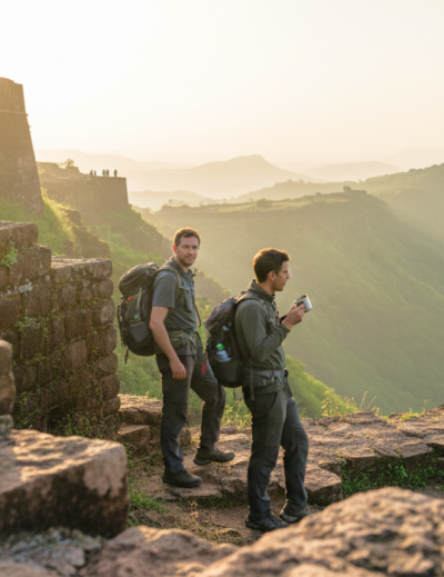 Two travellers with backpacks standing on the ramparts of Sinhagad Fort at sunrise, overlooking the misty Western Ghats — a highlight of any Pune itinerary thumbnail