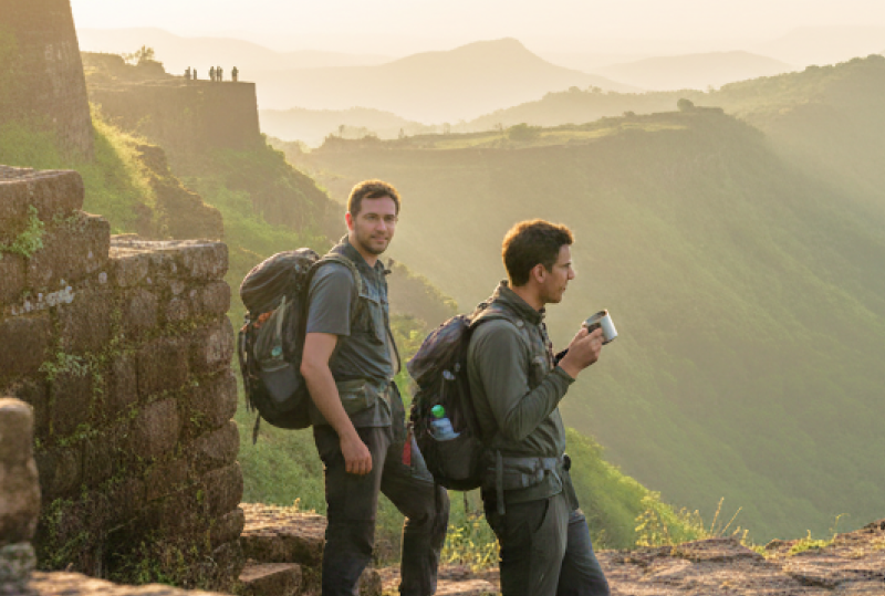 Two travellers with backpacks standing on the ramparts of Sinhagad Fort at sunrise, overlooking the misty Western Ghats — a highlight of any Pune itinerary thumbnail