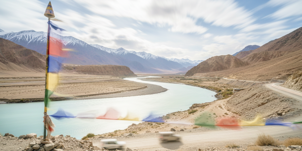 Tibetan prayer flags flutter over the turquoise Indus River winding through Ladakh's Himalayan landscape perfect for India summer travel