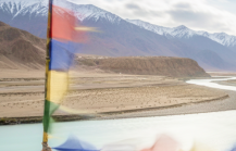 Tibetan prayer flags flutter over the turquoise Indus River winding through Ladakh's Himalayan landscape perfect for India summer travel thumbnail