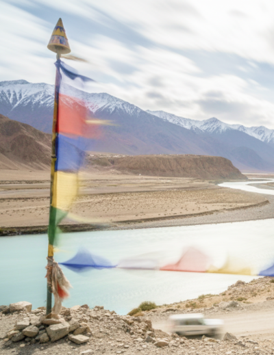 Tibetan prayer flags flutter over the turquoise Indus River winding through Ladakh's Himalayan landscape perfect for India summer travel thumbnail