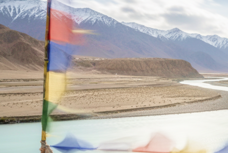 Tibetan prayer flags flutter over the turquoise Indus River winding through Ladakh's Himalayan landscape perfect for India summer travel thumbnail