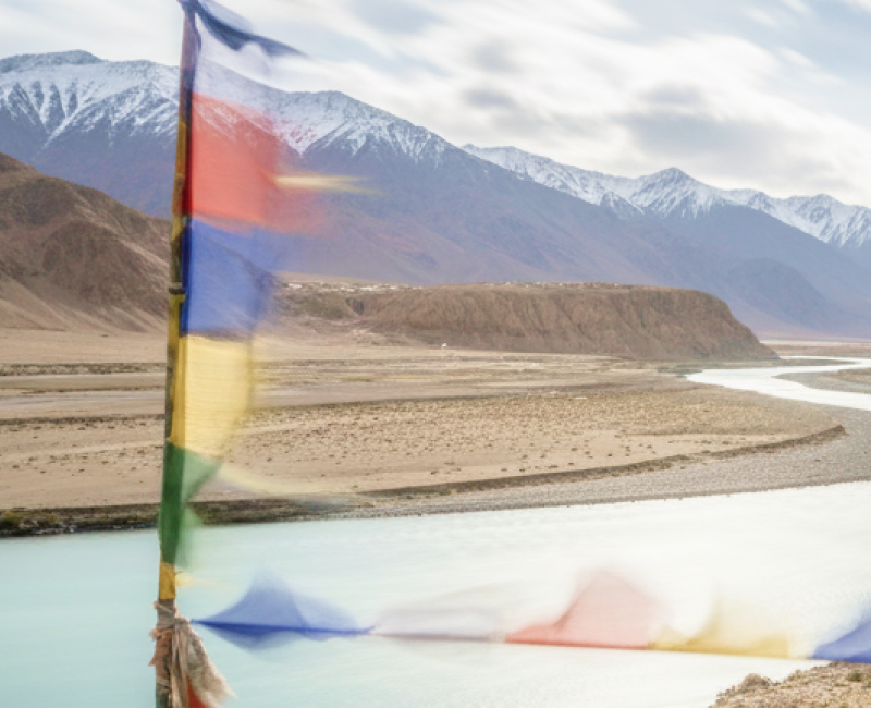 Tibetan prayer flags flutter over the turquoise Indus River winding through Ladakh's Himalayan landscape perfect for India summer travel thumbnail