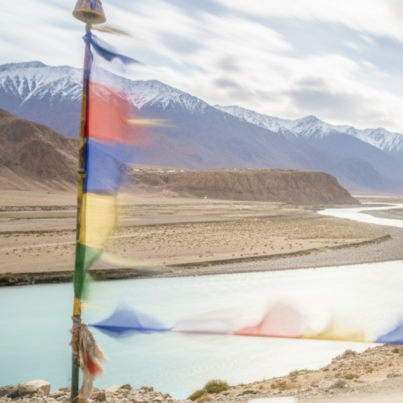 Tibetan prayer flags flutter over the turquoise Indus River winding through Ladakh's Himalayan landscape perfect for India summer travel thumbnail