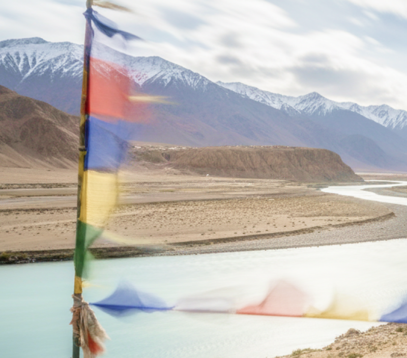 Tibetan prayer flags flutter over the turquoise Indus River winding through Ladakh's Himalayan landscape perfect for India summer travel thumbnail