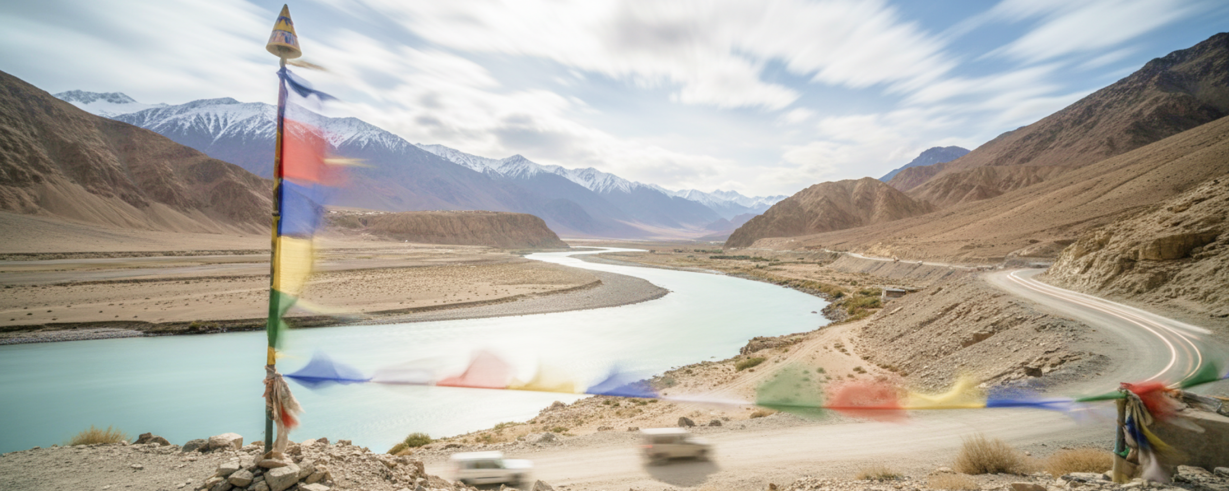 Tibetan prayer flags flutter over the turquoise Indus River winding through Ladakh's Himalayan landscape perfect for India summer travel