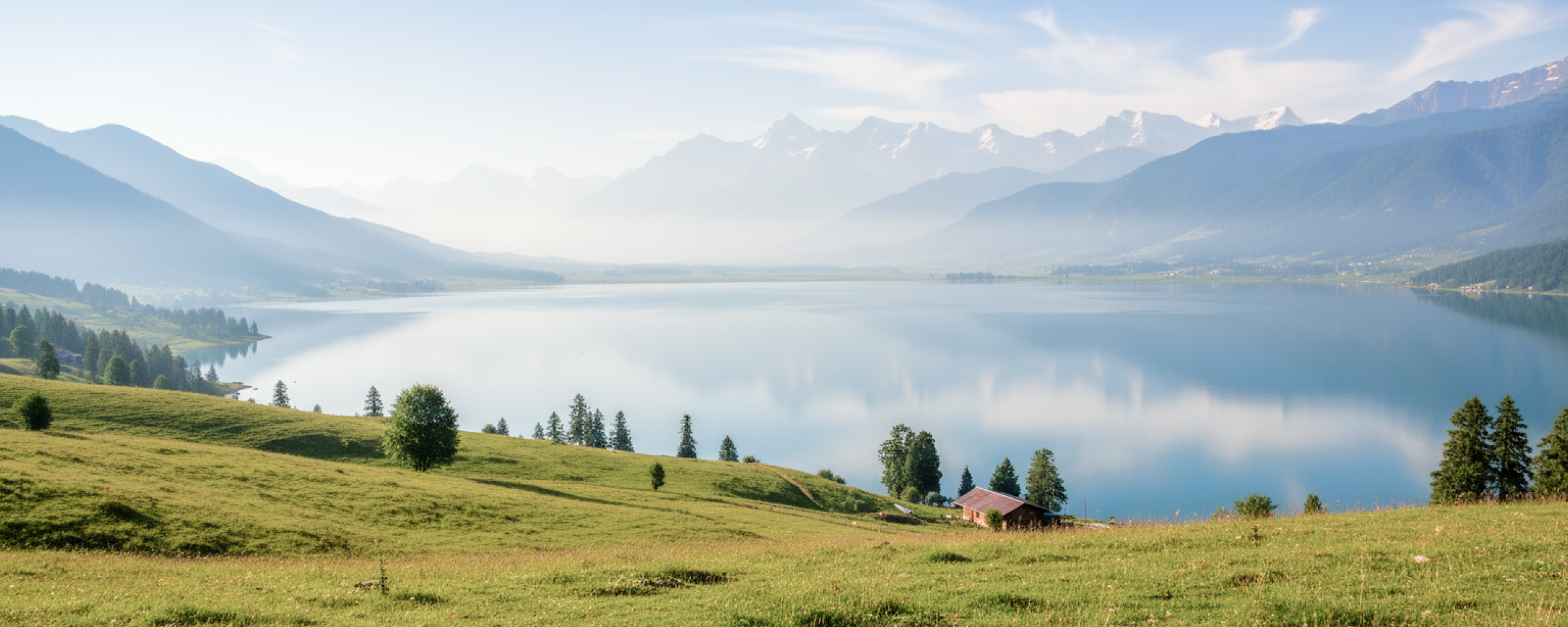 Panoramic view of a serene alpine lake surrounded by snow capped mountains and green meadows — Kashmir travel guide